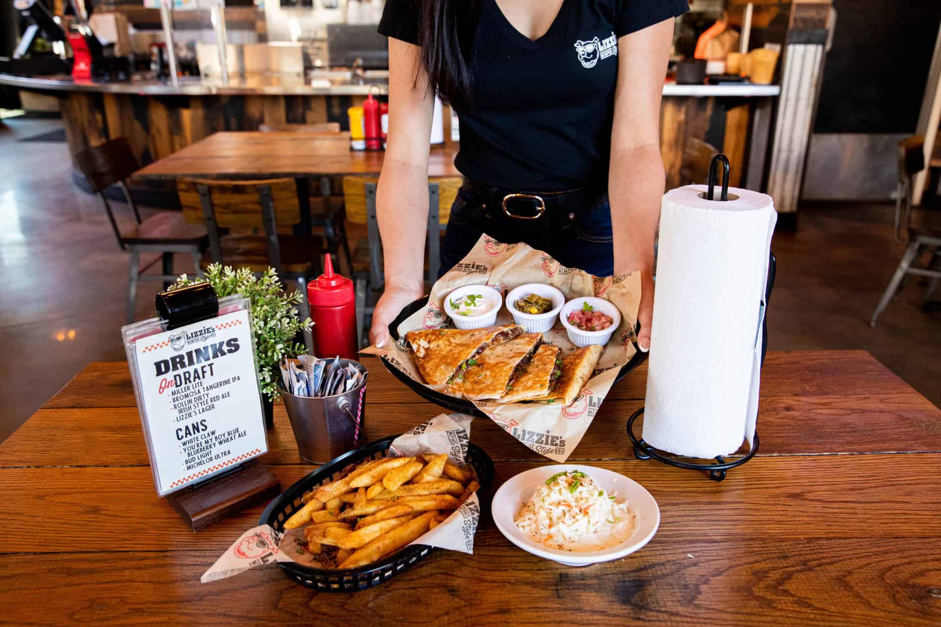 Server delivering Lizzie’s BBQ quesadilla to a table with fries and coleslaw