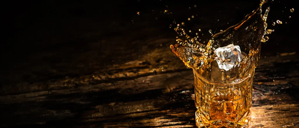 Ice cube splashing into a glass of bourbon whiskey